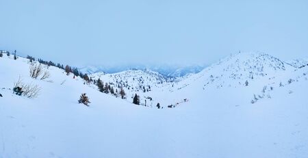 Panorama of winter Feuerkogel mountain plateau in snowstorm with misty Alpine peaks and white...
