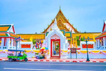 BANGKOK, THAILAND - APRIL 15, 2019: The tuk-tuk rickshaw stands at the open doors of the Wat Suthat temple with a view on inner courtyard of famous religion complex, on April 15 in Bangkokのeditorial素材