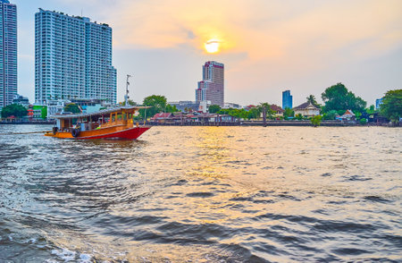 BANGKOK, THAILAND - APRIL 15, 2019: The old boat sails along Chao Phraya river in residential district at twilights, on April 15 in Bangkokのeditorial素材