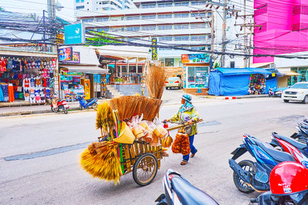 PATONG, THAILAND - APRIL 30, 2019: The street seller walks the market street with many straw brooms in her trolley cart, on April 30 in Patongのeditorial素材