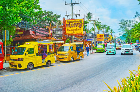 PATONG, THAILAND - APRIL 30, 2019: The driving and parked colorful mini buses, serving as the shared taxies in coastal street of resort, on April 30 in Patongのeditorial素材