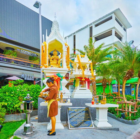 PATONG, THAILAND - APRIL 30, 2019: The waitress of local cafe makes food offerings at the altar of small mondop pavilion, located in garden of shopping mall, on April 30 in Patongのeditorial素材