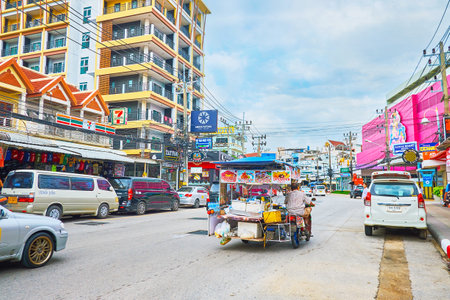 PATONG, THAILAND - APRIL 30, 2019: The traffic in busy street with a view on modern housing, market stalls and riding street food cart, ttached to the old bike, on April 30 in Patongのeditorial素材