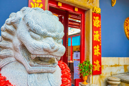 BANGKOK, THAILAND - APRIL 15, 2019: The amazing stone sculpture of the Chinese lion at the entrance to the Kwang Tung Shrine with inscriptions on the door frame, on April 15 in Bangkokのeditorial素材