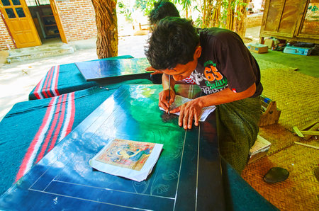 BAGAN, MYANMAR - FEBRUARY 25, 2018: The artisan creates the picture on lacquer panel, scratching it...