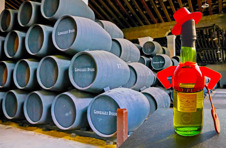 JEREZ, SPAIN - SEPTEMBER 20, 2019: The large hall of Bodegas Tio Pepe winery with stacked oak casks and Fino sherry bottle, decorated with hat, jacket and guitar, as Tio Pepe logo, on September 20 in Jerezのeditorial素材