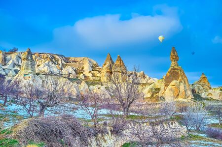 Mind-blowing landscape of Pifeon Valley with bright yellow tuff rocks, ancient caves, cut cells, orchards and flying hot air balloons, Pigeon Valley, Cappadocia, Turkeyの写真素材