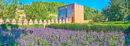 Panorama of Alhambra garden with rampart, topped with battlements, medieval Judge Tower (Torre del Cadi, Prisoners Tower) and blooming ultra violet salvia (sage), Granada, Spainの写真素材