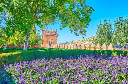 The picturesque Alhambra garden with flower bed of ultra violet salvia (sage), shady trees, preserved fortress wall and Tower of Points (Torre de los Picos) on the background, Granada, Spainの写真素材