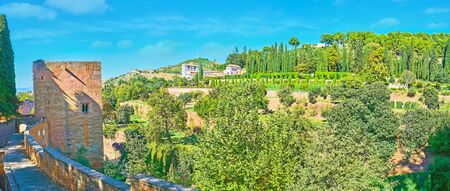 Panorama of lush green Generalife gardens, occupying the Sun Hill, and the medieval Tower of Captive (Torre de la Cautiva) on the left side, Alhambra, Granada, Spainの写真素材