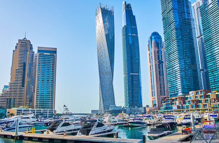 DUBAI, UAE - MARCH 2, 2020: The yacht club in front of the tallest skyscrapers of Dubai Marina - twisting Cayan Tower and Damac Residenze, on March 2 in Dubaiのeditorial素材