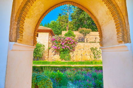 The carved Mudejar style arch opens the view on colorful flowers and lush greenery of Patio of Irrigation Ditch, Generalife, Alhambra, Granada, Spainのeditorial素材