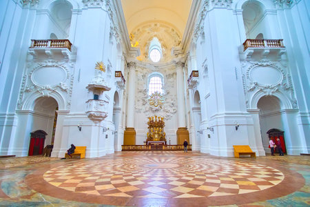 SALZBURG, AUSTRIA - MARCH 1, 2019: Interior of Collegiate Church with mosaic stone floor white carved decorated walls and wooden Altar on background, on March 1 in Salzburgのeditorial素材