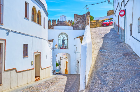 The zigzag hilly street with white houses, remains of medieval fortress wall and Martera gate, separating upper and lower town of Arcos, Spainのeditorial素材
