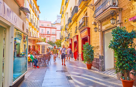 CADIZ, SPAIN - SEPTEMBER 23, 2019: The crowded Calle Columela street with tables of outdoor cafe, stores, classic edifices and plants in pots, on September 23 in Cadizのeditorial素材