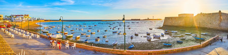 CADIZ, SPAIN - SEPTEMBER 23, 2019: Panorama of La Caleta harbor at sunset - the sun shines over the...