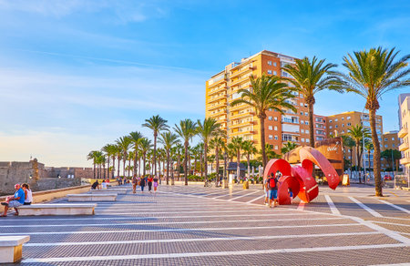 CADIZ, SPAIN - SEPTEMBER 23, 2019: The promenade of La Caleta beach with a view on modern Arroba sculpture, line of palm trees and modern houses on background, on September 23 in Cadizのeditorial素材