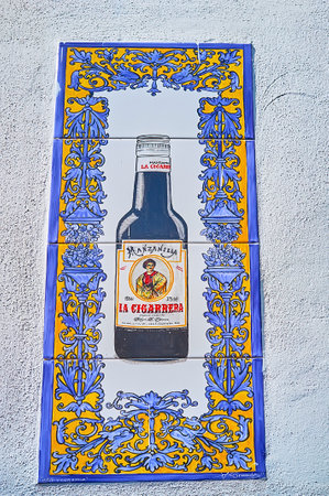 SANLUCAR, SPAIN - SEPTEMBER 22, 2019: The tile picture of Manzanilla Sherry wine bottle of Bodegas La Cigarrera winery in frame of bright Andalusian patterns, on September 22 in Sanlucarのeditorial素材
