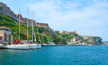The sea trip along the harbor of Bonifacio with a view on moored sail yachts and the limestone cliffs, topped with historic ramparts and towers of the Citadel, Corsica, Franceの写真素材