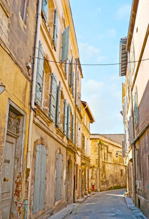 The narrow winding street in old town with historic buildings, shabby wooden doors and shutters, Arles, Franceの写真素材