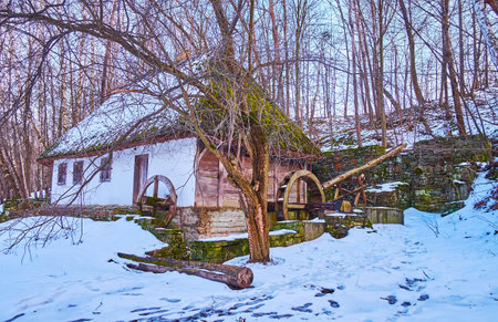 The snowy hill slope with a view on the timber whitewashed building of the water mill, Bukovyna Region architecture, Pyrohiv Skansen, Kyiv, Ukraineのeditorial素材