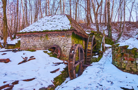 The old stone water mill at the foot of the snowy hill, surrounded with birch trees, Bukovyna Region architecture, Pyrohiv Skansen, Kyiv, Ukraineのeditorial素材