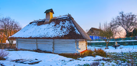 Panorama of the old whitewashed hata house with straw roof, covered with snow, Podillya Region architecture, Pyrohiv Skansen, Kyiv, Ukraineのeditorial素材