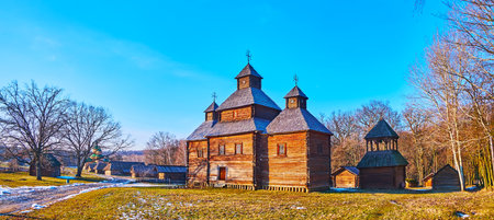Panorama of the timber Resurrection Church with belfry, snowy lawn and the farmhouses of Polissya region, Pyrohiv Skansen, Kyiv, Ukraineのeditorial素材