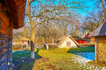 The green yard of the small farmstead with a view on barns, pens, storages and a small clay root cellar, Pyrohiv Skansen, Kyiv, Ukraineのeditorial素材