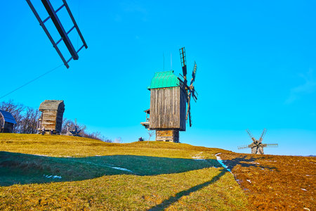 The green spring meadow with reminds of the last snow and a view of historic wooden windmills,...