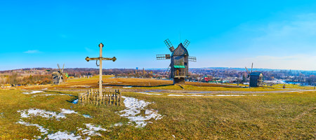 Panorama of Pyrohiv Skansen landscape with green hilly meadow, old cross and historic wooden windmills, Kyiv, Ukraineのeditorial素材