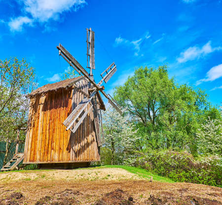 The vintage wooden windmill on the hill among the lush spring greenery, Mamajeva Sloboda Cossack Village, Kyiv, Ukraineの写真素材