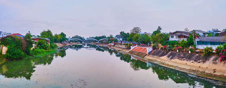 Panorama of the Wang River with clear surface, reflecting the banks with greenery and old housing of Lampang, Thailandの写真素材