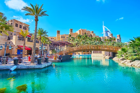 Park area of Souk Madinat Jumeirah market complex with canal, pedestrian bridge, lush greenery, Fort Island, cafes and Burj Al Arab in background, Dubai, UAEのeditorial素材