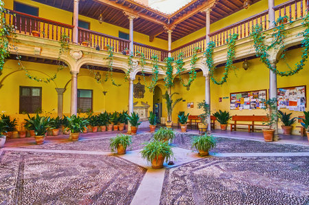 GRANADA, SPAIN - SEPT 27, 2019: The scenic courtyard of Victoria Eugenia Royal Conservatory of Music, decorated with mosaic on the floor, stone columns and plants in pots, on Sept 27 in Granadaのeditorial素材
