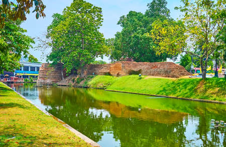 The beautiful green park, reflecting on waters of Old City Moat Canal with a view on ruins of the city fortress on the opposite bank, Si Phum Corner, Chiang Mai, Thailandの写真素材