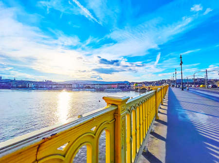 The evening walk along the Margaret Bridge with bright yellow rails and a view of the colorful sky...