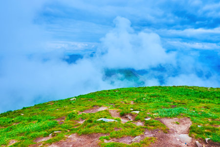 The picturesque green mountain landscape from Mount Hoverla peak with swirling low clouds in the...