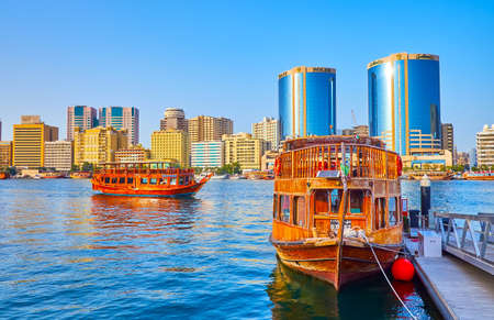 DUBAI, UAE - MARCH 1, 2020: The dhow boat is moored at the pier on Dubai Creek with a view on Deira bank with modern housing and Deira Twin Towers (Rolex Towers), on March 1 in Dubaiのeditorial素材