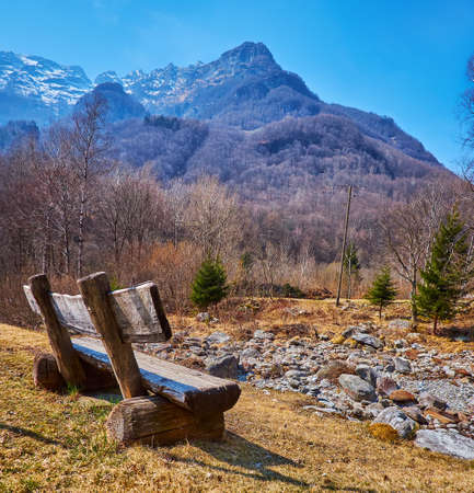 The old timber bench at the shallow Riale Efra River with a view of Poncione della Marcia Mount in the background, Frasco, Valle Verzasca, Switzerlandの写真素材
