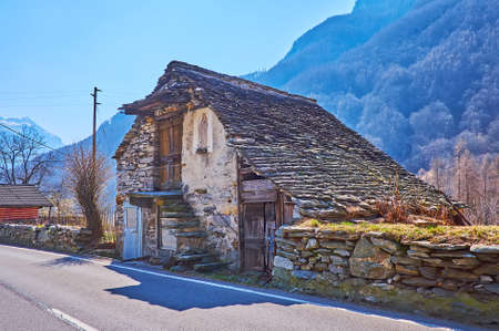 The small abandoned stone house with stone covered roof and small chapel of Virgin Mary on the facade wall, Mora di Fuori, Valle Verzasca, Switzerlandのeditorial素材