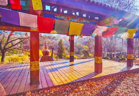 The sunny autumn midday in Tibetan Garden with Buddhist flags, gazebo for meditation and Chorten in...