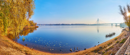 The foggy sunrise on Dnieper River with a view on the silhouette of Pivnichnyi (Northern) Bridge behind the sand river's bank, Kyiv, Ukraineの写真素材