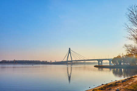 The early morning on Dnieper River with a view on bright sunrise sky, Pivnichnyi (Northern) Bridge and plants in autumn colors, Kyiv, Ukraineの写真素材