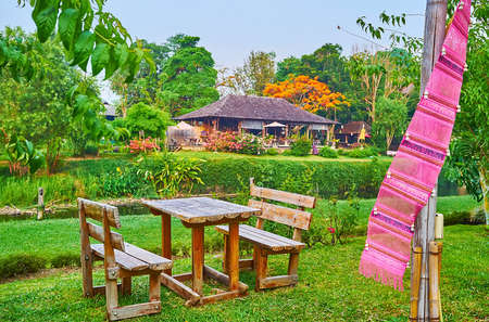 The small wooden terrace with colorful Lanna flag and wooden tables and chairs on the green bank of Pai River, Pai, Thailandの写真素材