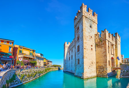 SIRMIONE, ITALY - APRIL 10, 2022: The main historic landmark of Sirmione - Castello Scaligero with moat and colored houses of Via Dante street around it, on April 10 in Sirmioneのeditorial素材