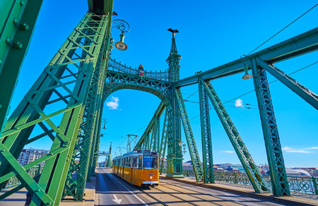 The yellow tram, riding on the Liberty Bridge with beautiful bright green metal elements, Budapest,...