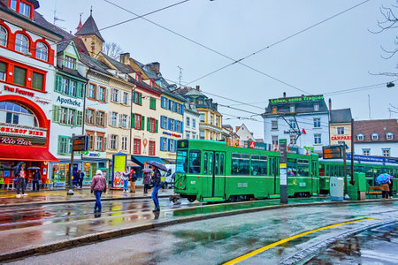 BASEL, SWITZERLAND - APRIL 1, 2022: The green tram riding on Barfusserplatz sqaure on cold rainy day, on April 1 in Basel, Switzerlandのeditorial素材