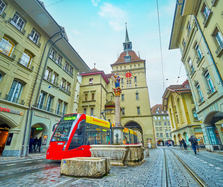 BERN, SWITZERLAND - MARCH 31, 2022: Red tram on Marktgasse street passing medieval...