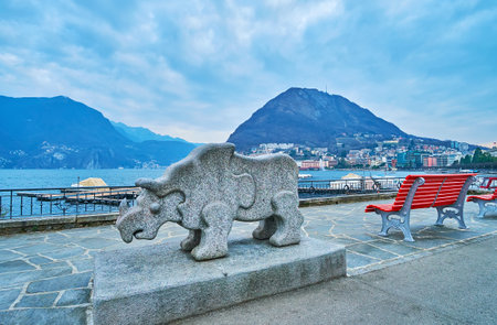 LUGANO, SWITZERLAND - MARCH 14, 2022: The stone statue of Rhinoceros in Park of Sculptures on embankment of Lake Lugano with Monte San Salvatore in background, Lugano, Switzerlandのeditorial素材